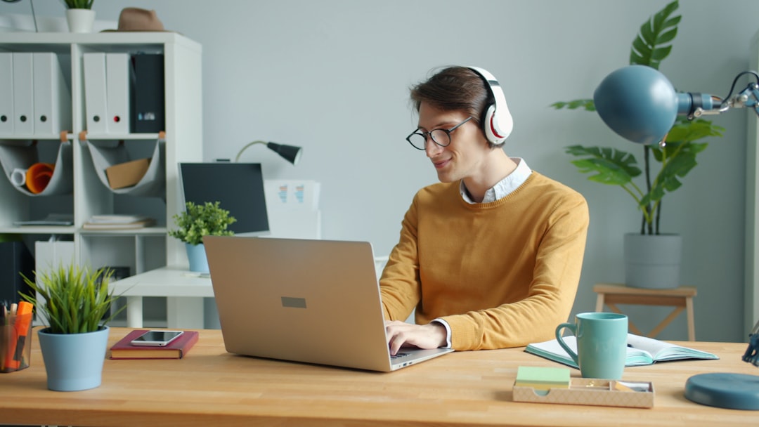 Man wearing headphones working on laptop at desk person working from home, laptop healthcare coding, home office workspace, relaxed professional