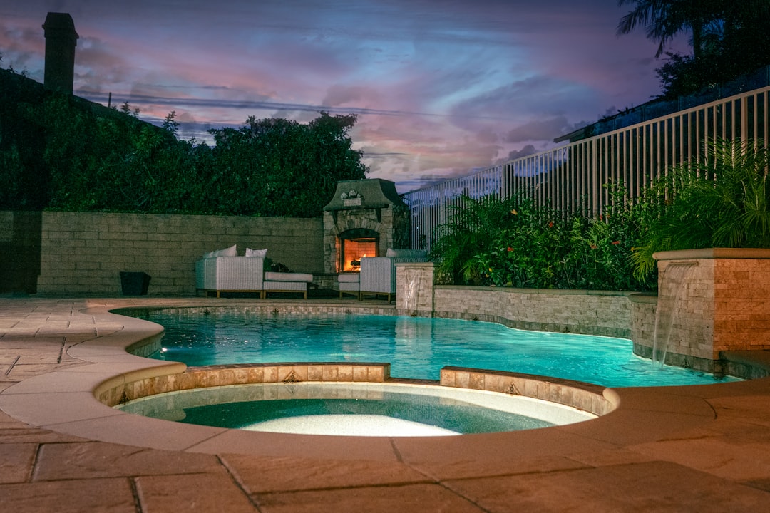 a swimming pool with a building in the background heated plunge pool at night, outdoor lighting, steam rising water, cozy backyard