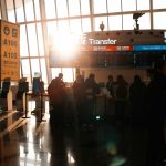 People in airport terminal with sun flare traveler swapping sim card, smartphone close up, airport setting