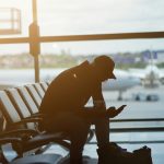 a man sitting at an airport looking at his cell phone smartphone esim setup screen travel airport