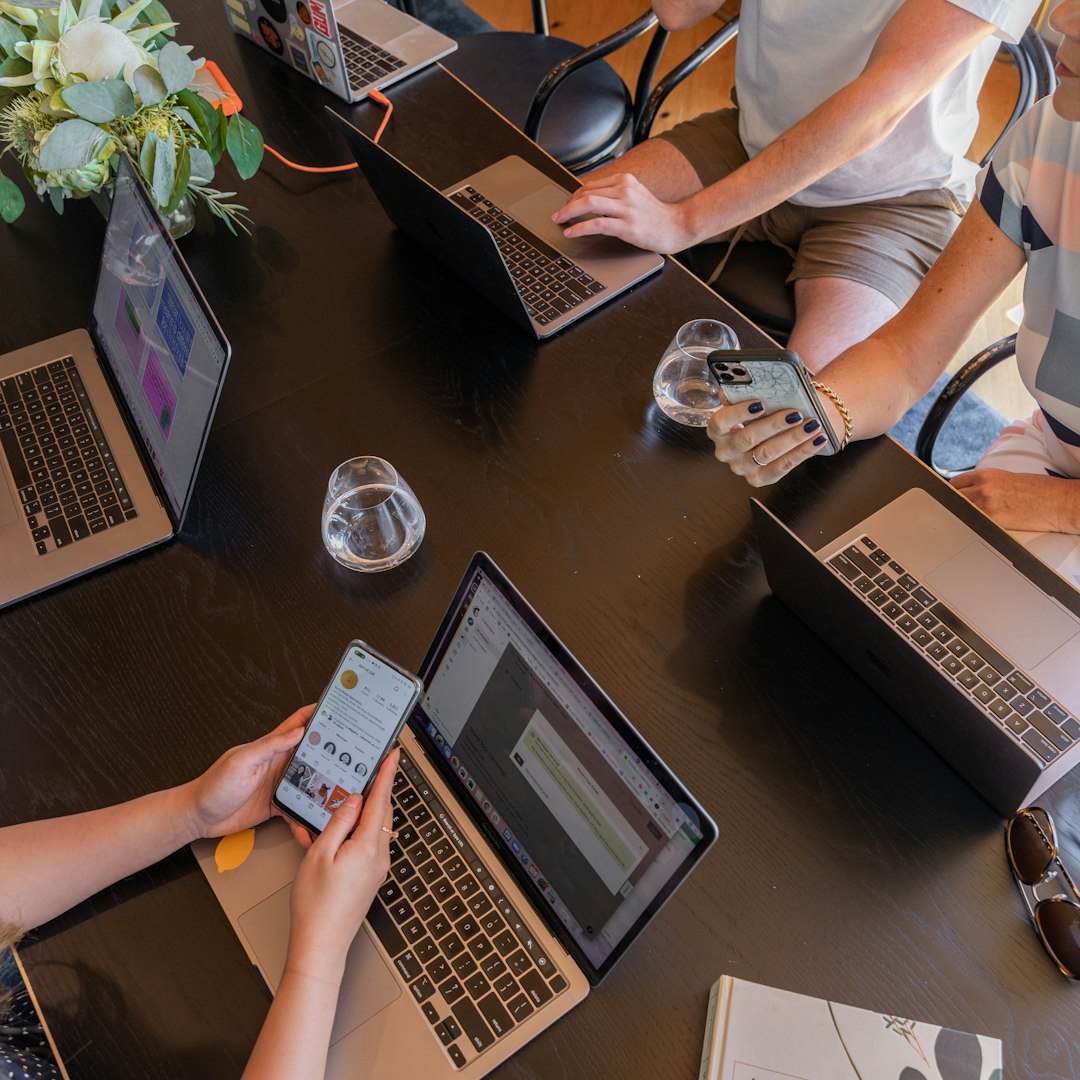 a group of people sitting around a table with laptops digital collaboration workspace laptops strategy meeting