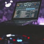black laptop computer turned on on black table virtual dj interface screen, waveform mixing display, home studio dj setup, laptop dj software