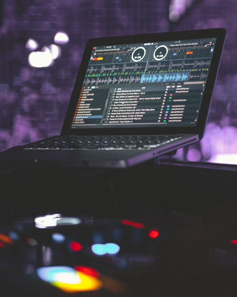black laptop computer turned on on black table virtual dj interface screen, waveform mixing display, home studio dj setup, laptop dj software