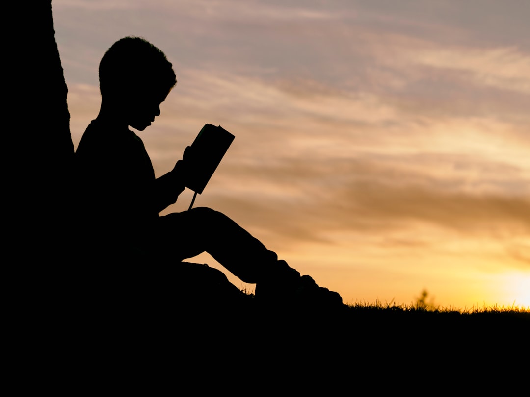 silhouette of child sitting behind tree during sunset child reading tablet, books, focused learning