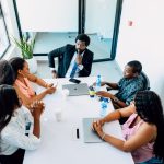 A group of people sitting around a white table business team reviewing analytics, digital contract management, collaborative workspace