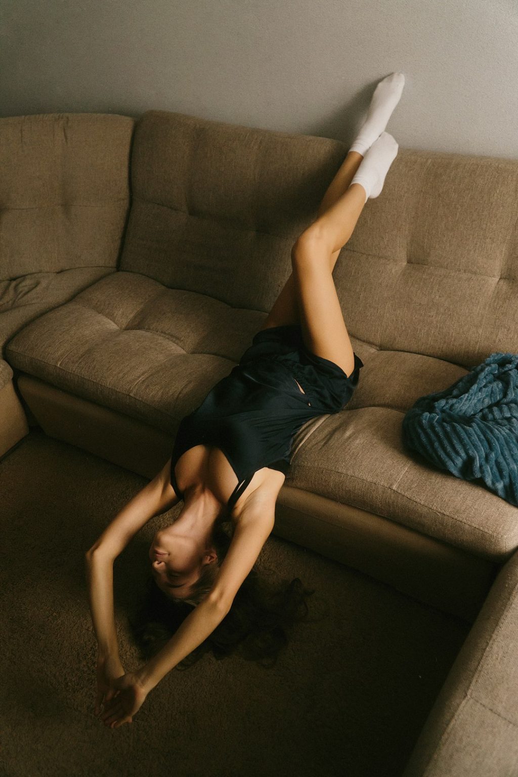 A woman laying on her back on a couch person stretching at home, herbal supplement, wellness routine