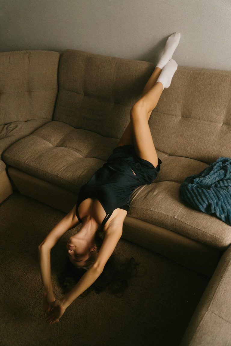 A woman laying on her back on a couch person stretching at home, herbal supplement, wellness routine