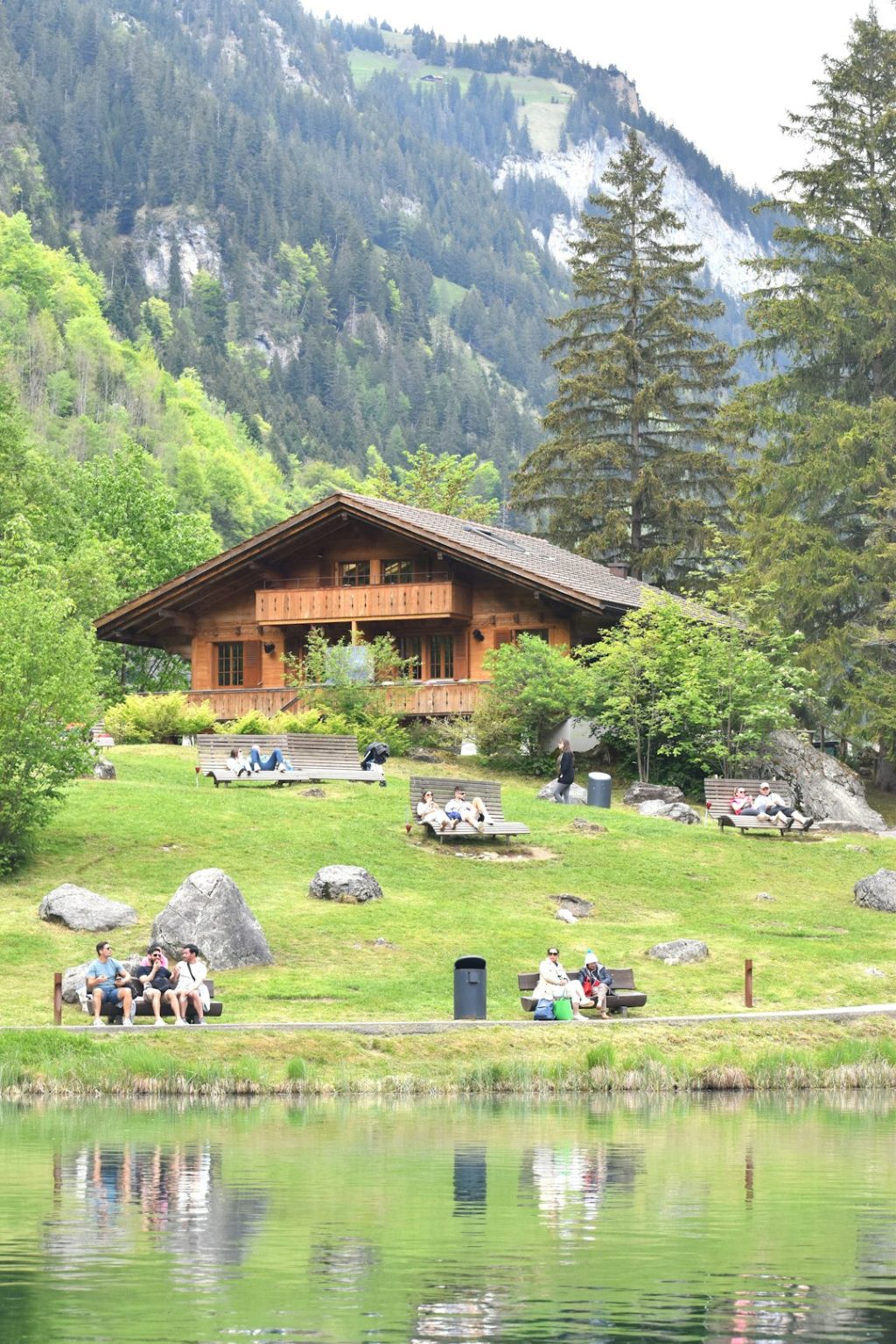 a group of people sitting on a bench in front of a lake traditional gathering, cultural clothing, mountain landscape, community celebration