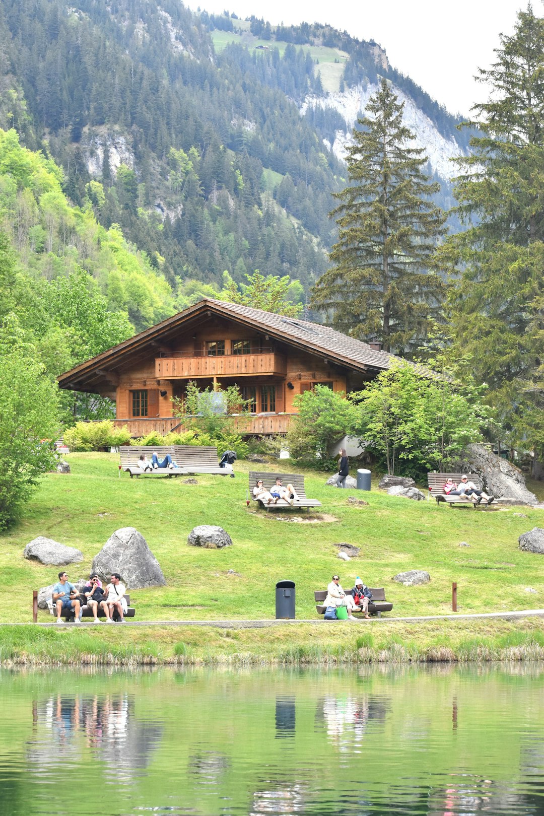a group of people sitting on a bench in front of a lake traditional gathering, cultural clothing, mountain landscape, community celebration