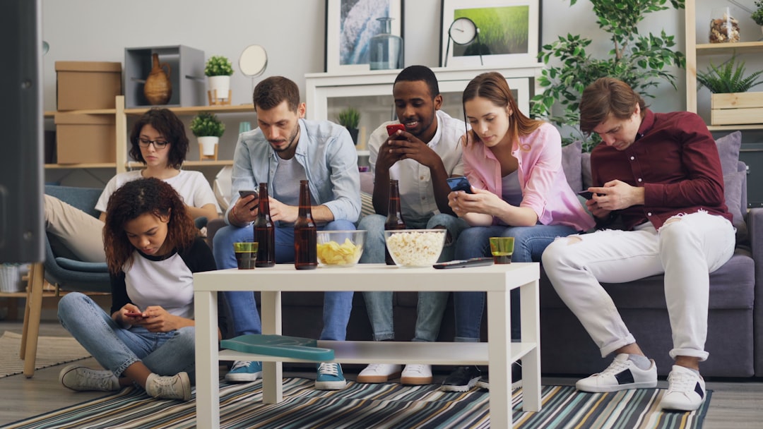 a group of people sitting on a couch looking at their phones diverse group laughing at phone, online connection, viral trend discussion