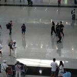 a group of people walking around a building person using laptop in airport, streaming video, travel suitcase nearby