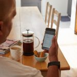 a man sitting at a table holding a smart phone customer support chat, mobile app interface, user engagement analytics