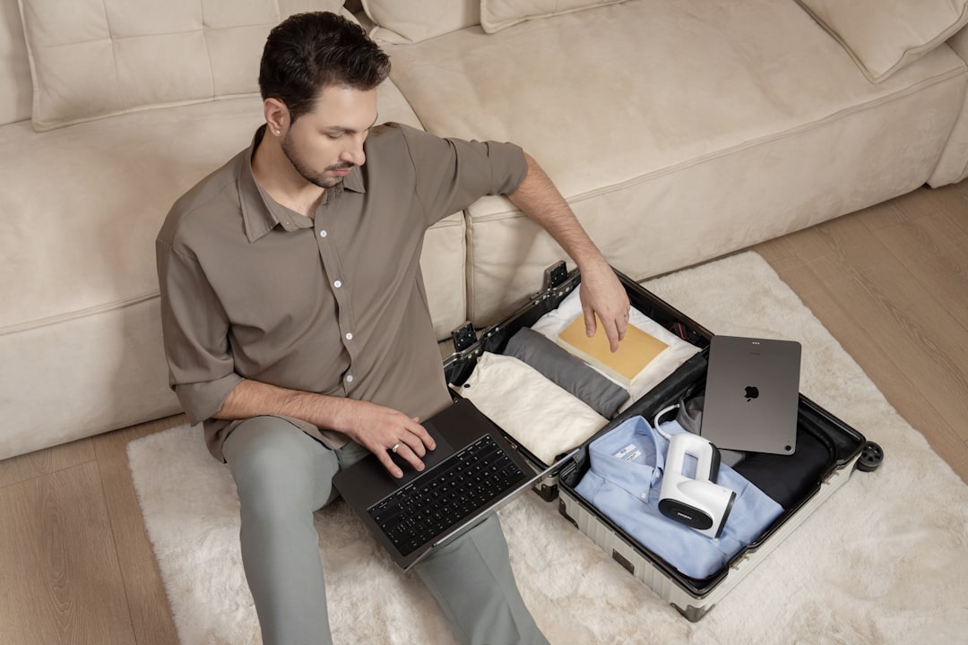 A man sitting on a couch using a laptop computer insurance claim documents, laptop with inventory report, house damage background