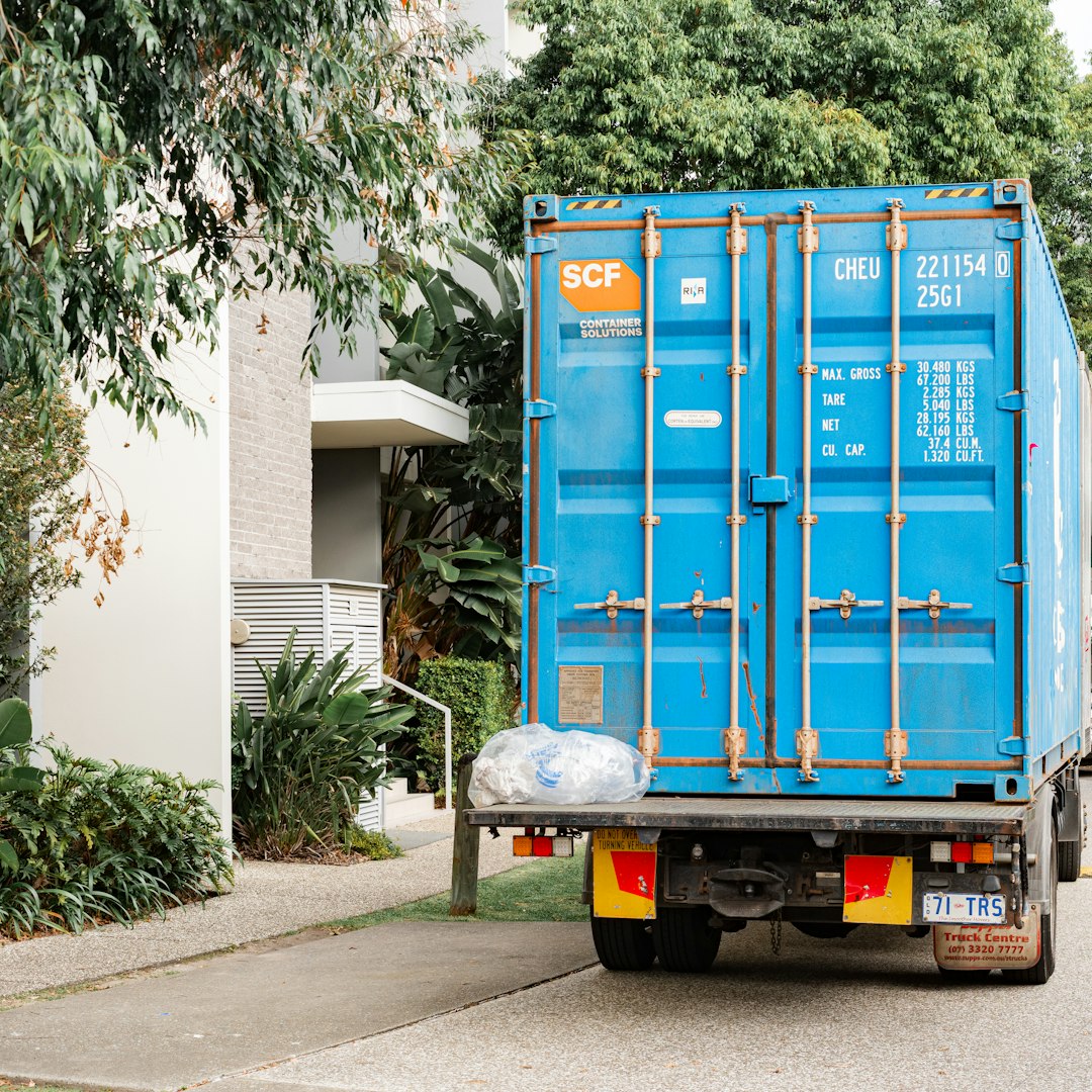 Blue shipping container on a truck parked by a building. moving boxes stacked, movers loading truck, residential relocation