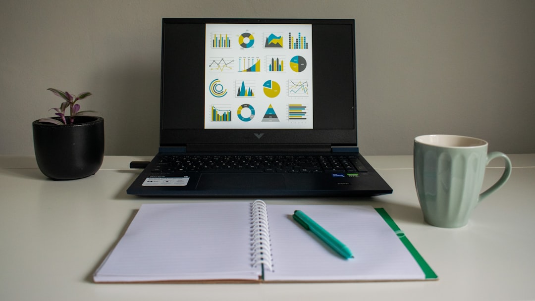 Laptop displaying charts next to notebook and mug. plagiarism report screen, laptop writing desk, content editing software