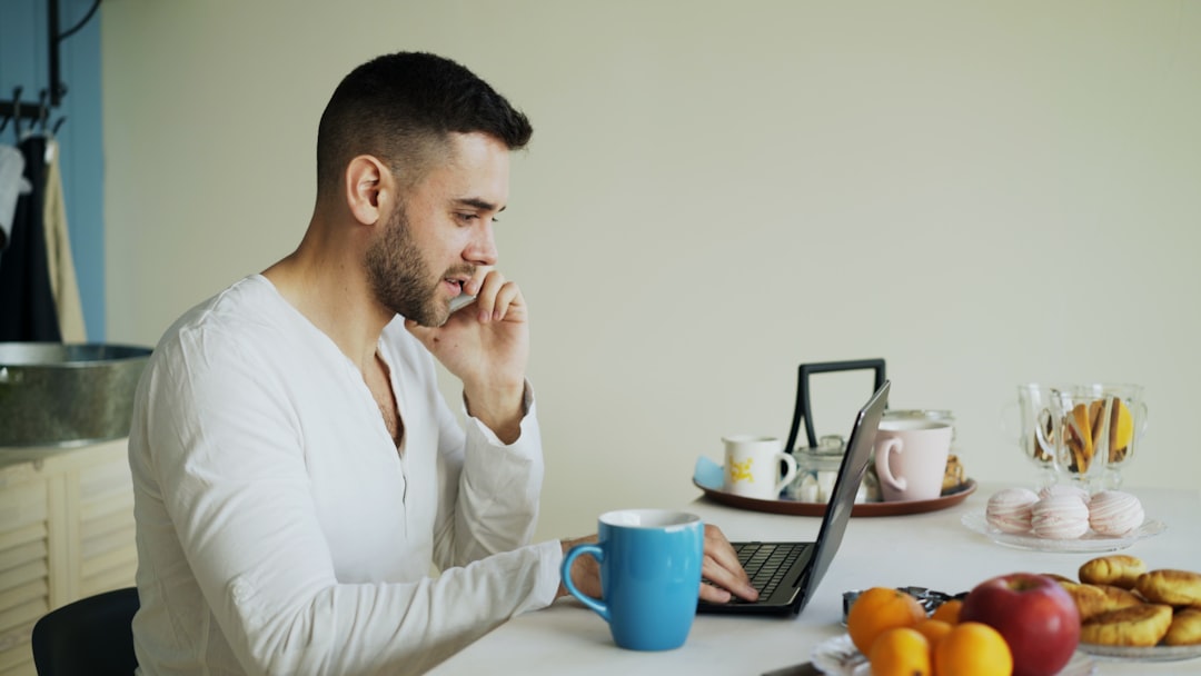 Man talking on phone while working on laptop at laptop person working from home signing digital documents, secure online verification, laptop and coffee table
