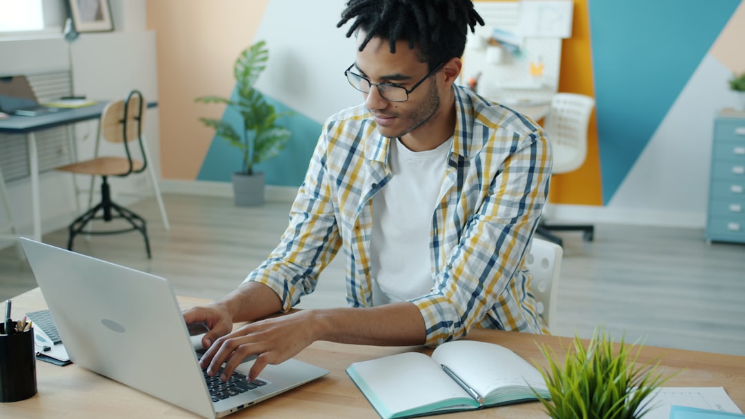 Man typing on laptop at a desk with notebook. person searching jobs on laptop at home office, notebook and coffee on desk, focused workspace