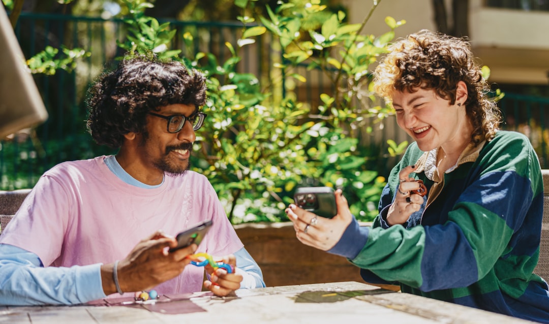 Two autistic friends sitting outside using stim toys and laughing at their phones diverse group laughing at phone, online connection, viral trend discussion