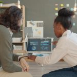Two people looking at data on a laptop screen diverse tech team meeting, laptops collaboration, modern office workspace, software development discussion