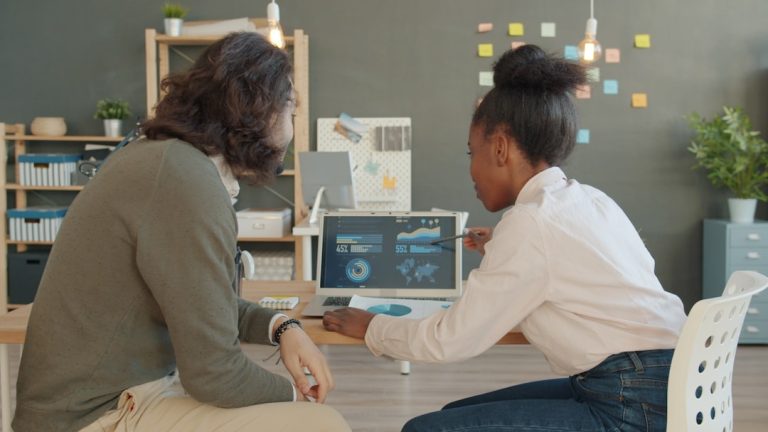 Two people looking at data on a laptop screen diverse tech team meeting, laptops collaboration, modern office workspace, software development discussion