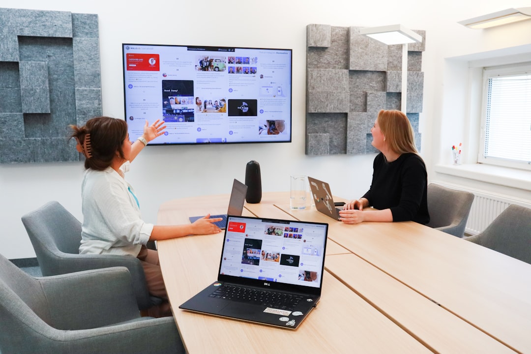 two women sitting at a table with a laptop business communication platform, team video meeting, shared documents screen, office collaboration