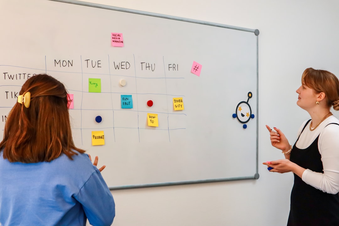 two women standing in front of a whiteboard with sticky notes on it creative review dashboard, marketing team collaboration, online proofing interface