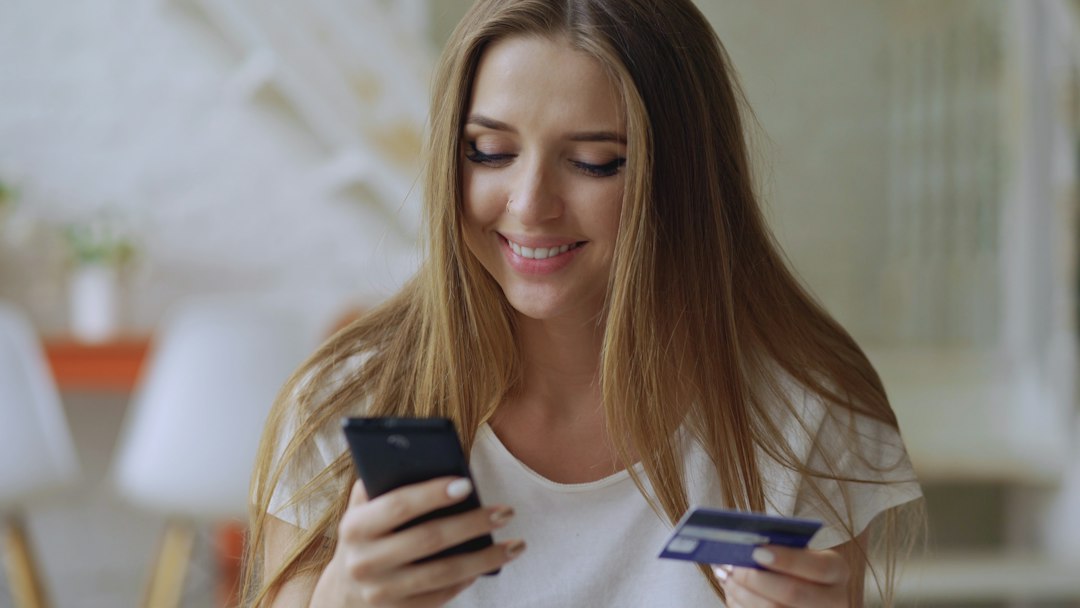 Young woman smiling while holding phone and credit card family phone plan, account management, online payment