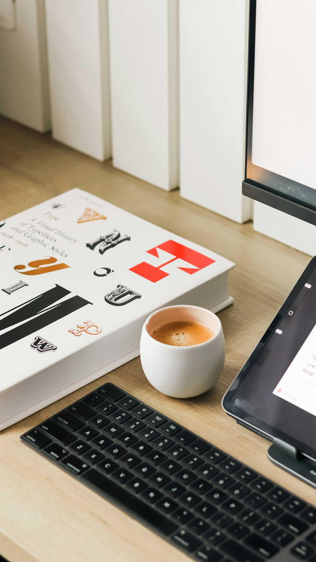 A book, coffee, and keyboard on a desk. organized home office desk, tablet with inventory app, household items neatly arranged