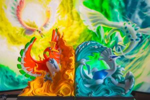 A couple of figurines sitting on top of a table dragon pokemon using powerful attack, glowing blue energy, battle arena minecraft