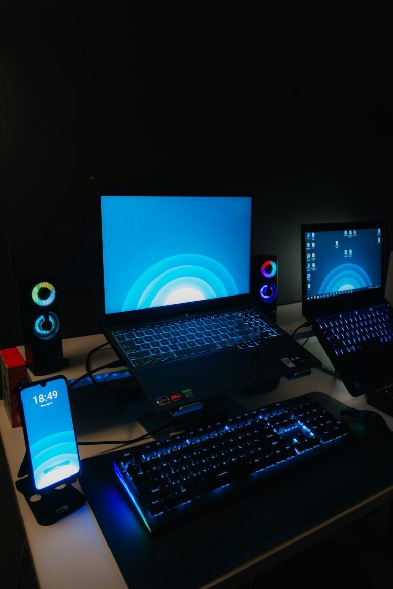 a desk with a laptop, monitor, keyboard and cell phone on it gaming pc setup, blue screen error, gamer desk