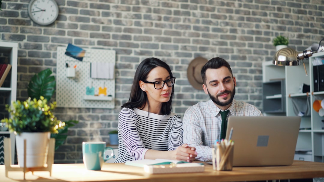 a man and woman sitting at a table looking at a laptop business team analyzing marketing budget on laptop