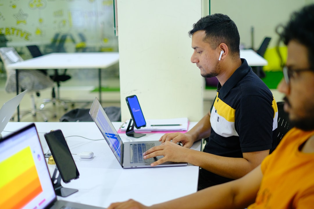 man in black and yellow polo shirt using macbook pro team reviewing laptop discussing marketing strategy office