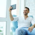 Man sitting in chair taking selfie with tablet real estate agent recording video message, smartphone marketing, client communication