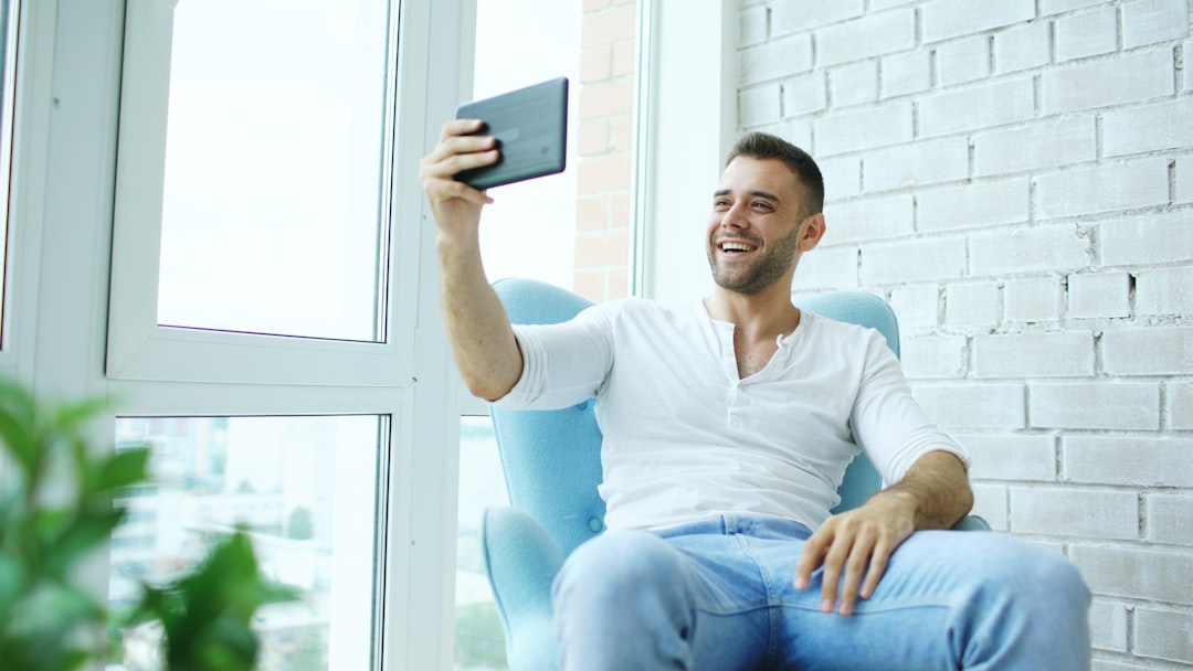 Man sitting in chair taking selfie with tablet real estate agent recording video message, smartphone marketing, client communication