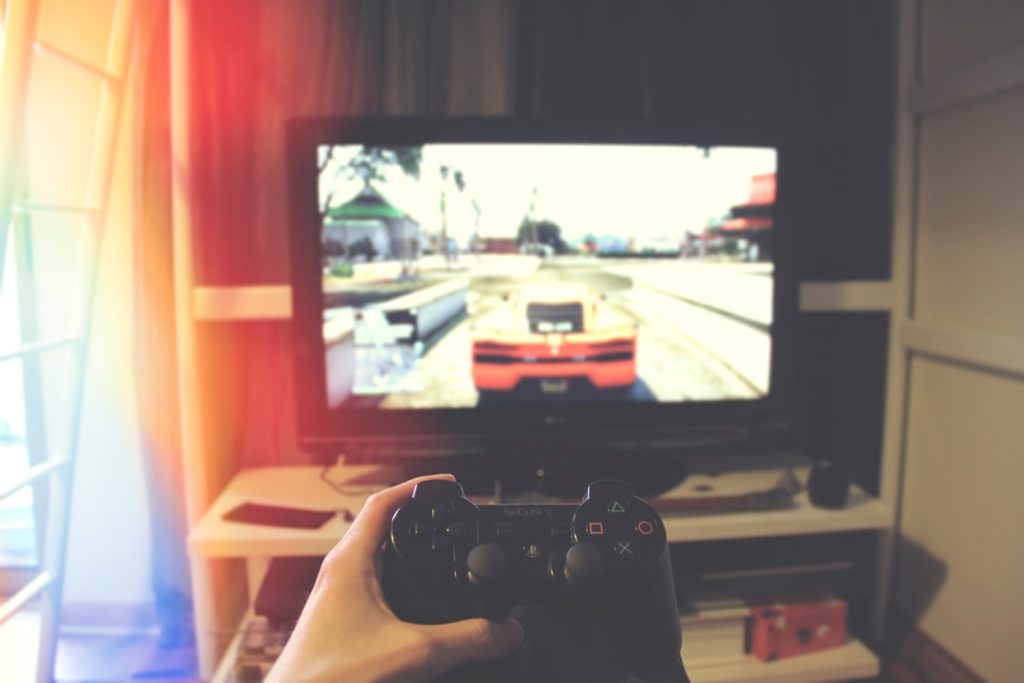 person holding Sony PS3 controller in front of flat screen monitor handheld console gaming screen, high resolution gameplay, vivid graphics display