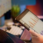 Someone analyzes financial data on a tablet. dashboard financial graphs charts laptop screen modern office