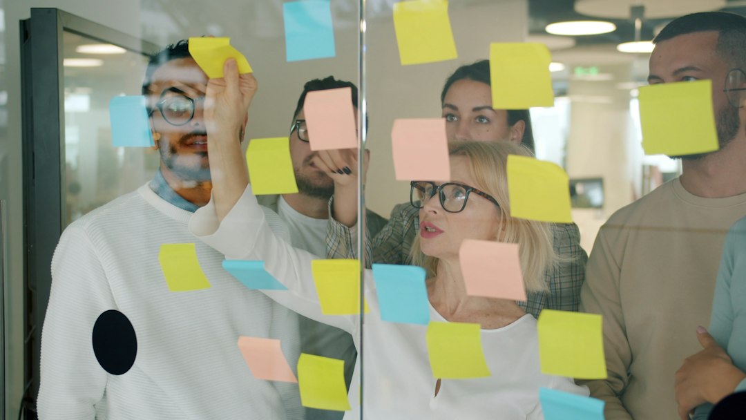 Team brainstorming with sticky notes on glass wall team voting, whiteboard, name ideas, happy coworkers