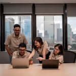 Team collaborating on laptops in modern office team reviewing laptop discussing marketing strategy office