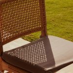 Woven chair with cushioned seat on grass outdoor patio carpet, balcony rug, modern terrace furniture