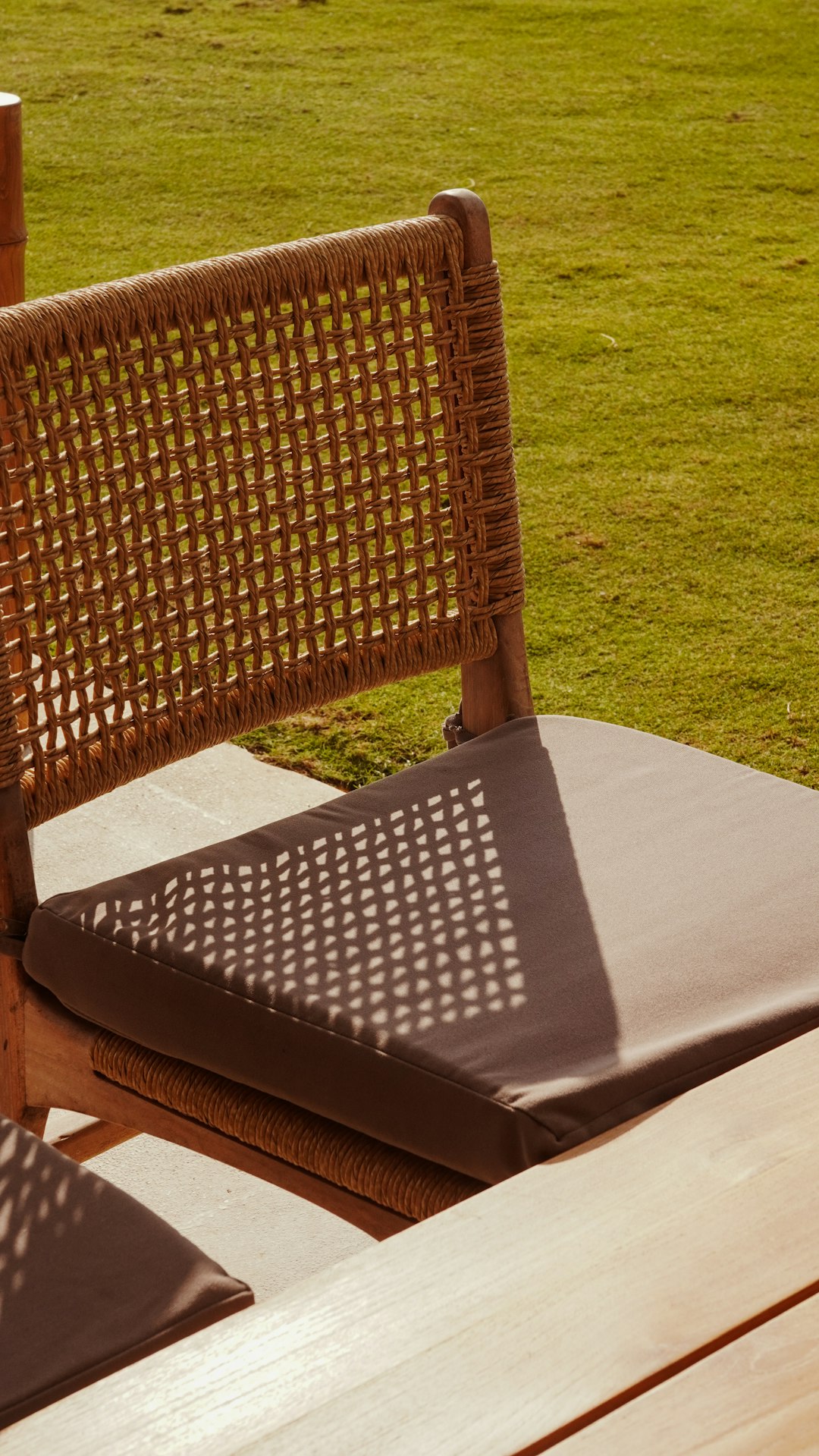 Woven chair with cushioned seat on grass outdoor patio carpet, balcony rug, modern terrace furniture