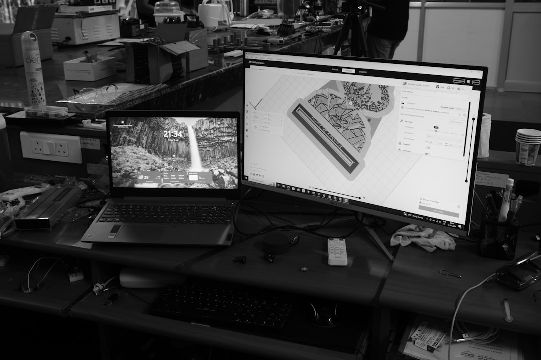 A black and white photo of a desk with two monitors team collaborating on 3D model, cloud based design software, multiple screens workspace