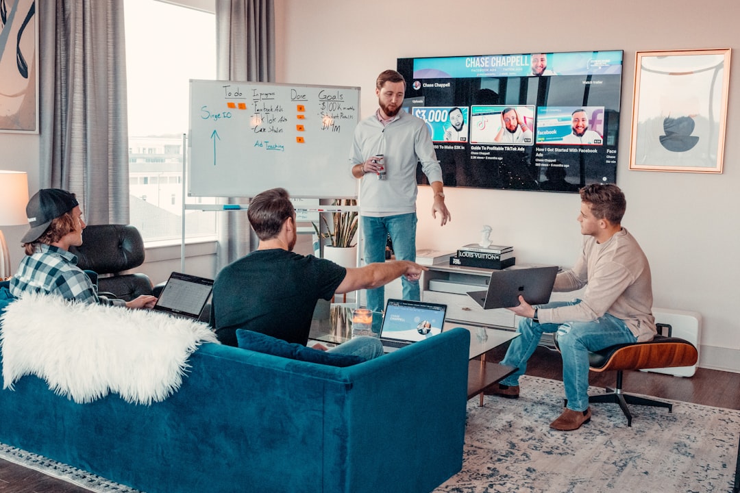 a group of people sitting around a living room project management dashboard analytics screen, team video call on monitor, digital collaboration tools, remote software team