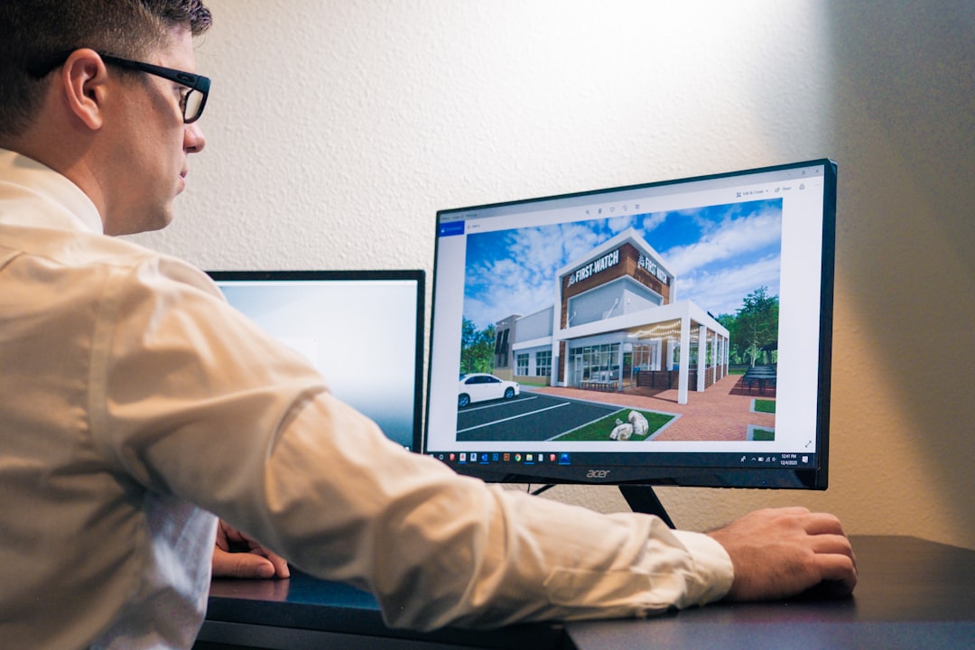 a man sitting at a desk looking at a computer screen architect using 3D modeling software, house design model, digital blueprint on screen