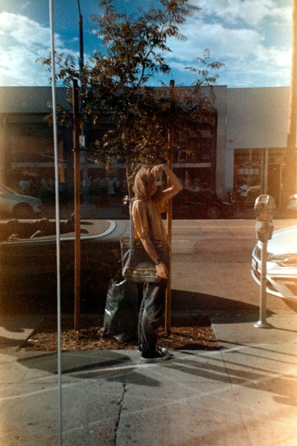 A man standing on a sidewalk next to a pole 1970s California suburb, teenage girl portrait, vintage sunlight