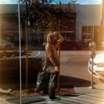 A man standing on a sidewalk next to a pole 1970s California suburb, teenage girl portrait, vintage sunlight