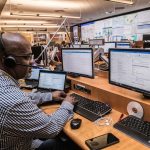 man in black and white checkered dress shirt using computer emergency operations center, multiple monitors, crisis response team