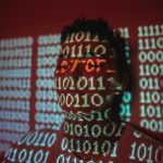 man in black and white checkered shirt cyber attack illustration, hacker at computer, red warning screen