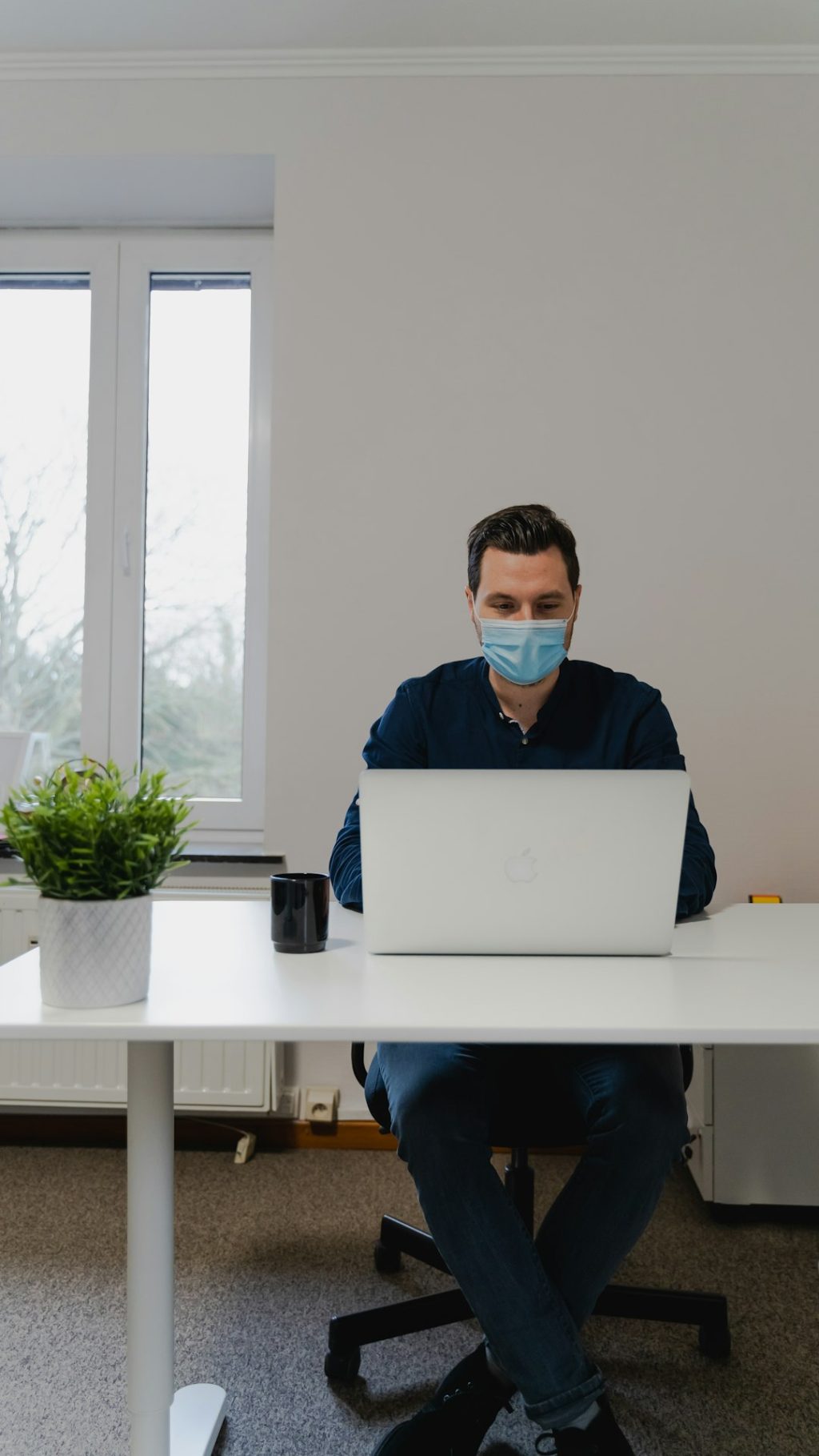 man in blue dress shirt using silver macbook remote work setup laptop security shield icon office environment