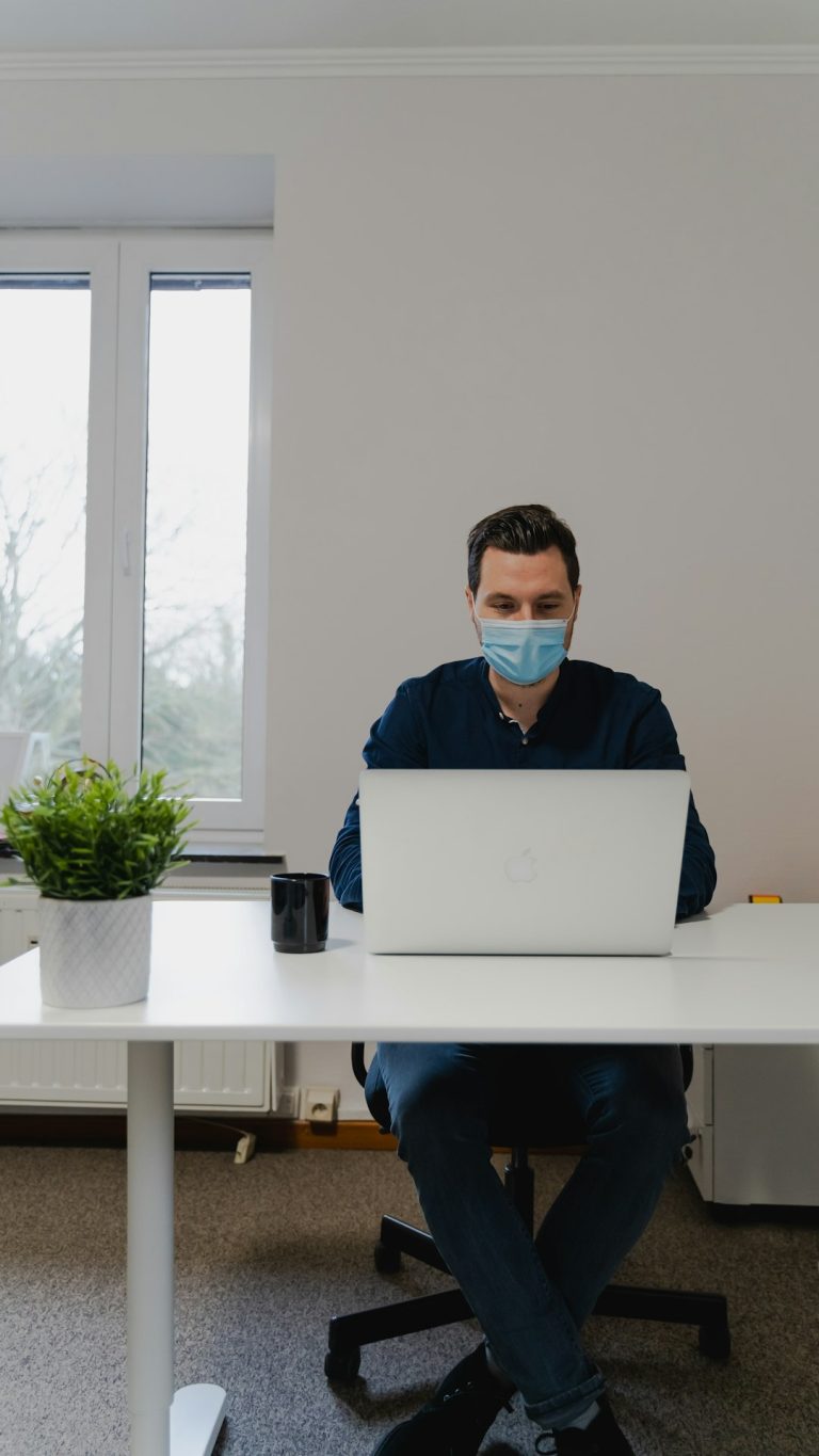 man in blue dress shirt using silver macbook remote work setup laptop security shield icon office environment
