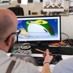 man in white shirt wearing black framed eyeglasses team collaborating on 3D model, cloud based design software, multiple screens workspace